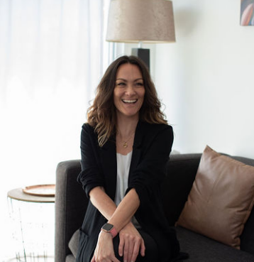 Marisa De Salvo, founder of The Five, sitting on a couch and smiling